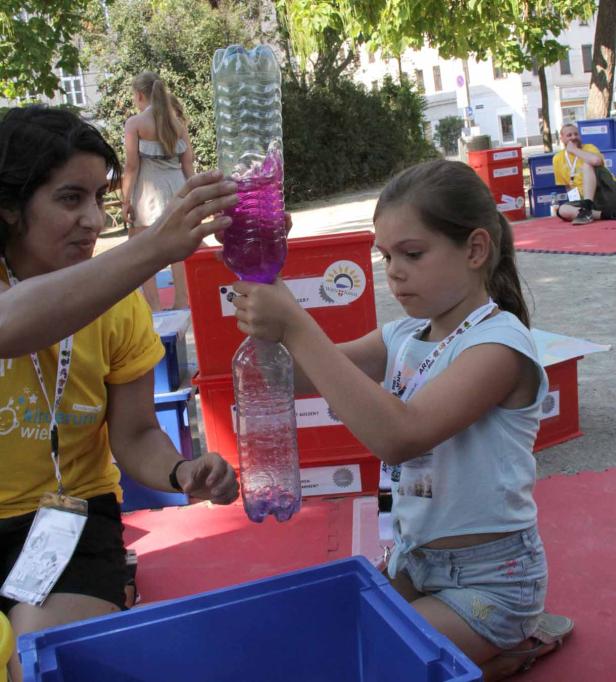 Ein Mädchen und eine Frau hantieren mit zwei mit Flüssigkeit gefüllten Plastikflaschen.