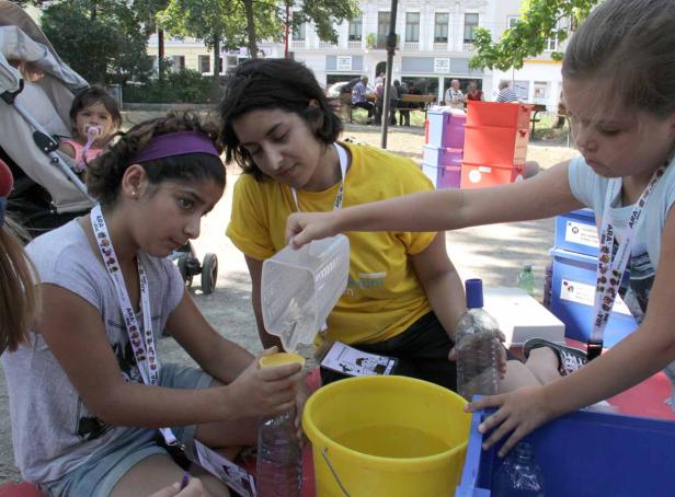 Kinder und eine Betreuerin experimentieren mit Wasser und Plastikflaschen im Freien.