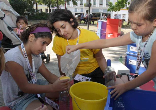 Kinder und eine Betreuerin experimentieren mit Wasser und Behältern im Freien.