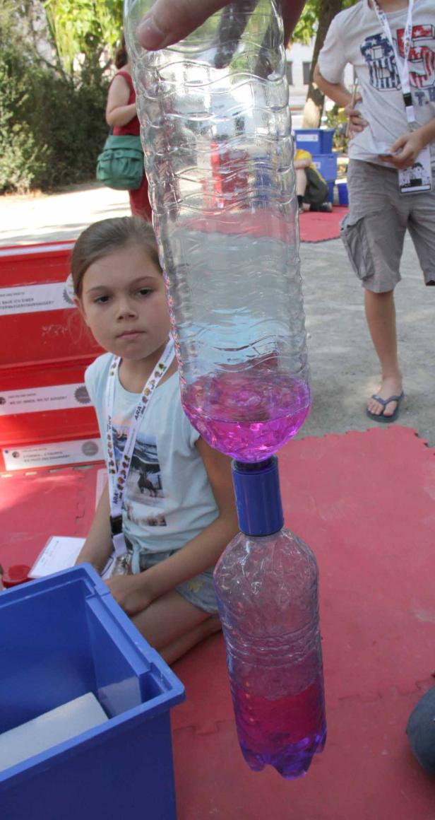 Ein Mädchen beobachtet, wie Wasser von einer Plastikflasche in eine andere fließt.