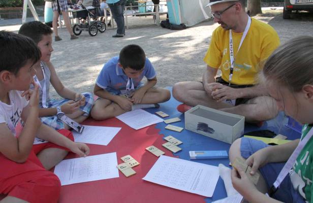 Eine Gruppe Kinder und ein Erwachsener sitzen auf einer Matte und lernen Blindenschrift.