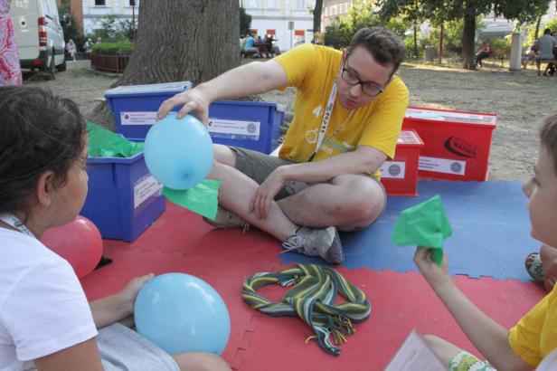 Ein Mann mit Brille verteilt blaue Luftballons an Kinder im Freien.
