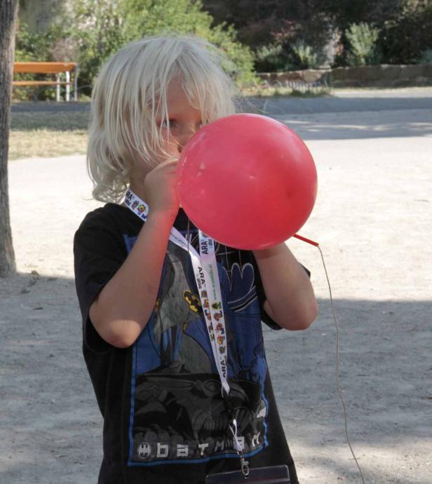 Ein Junge mit blonden Haaren bläst einen roten Ballon auf.