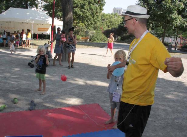 Ein Mann mit Hut spielt mit zwei Kindern im Park mit Ballons.