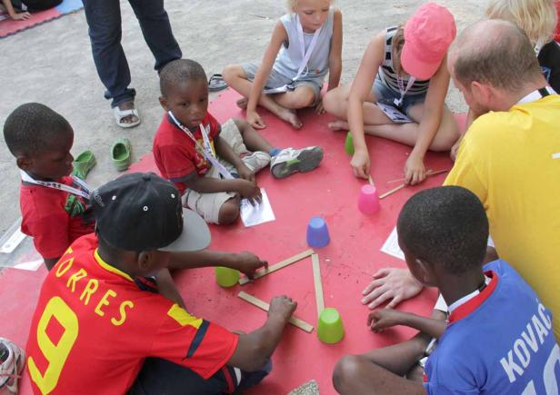 Eine Gruppe Kinder sitzt auf dem Boden und spielt mit Bechern und Holzstäben.