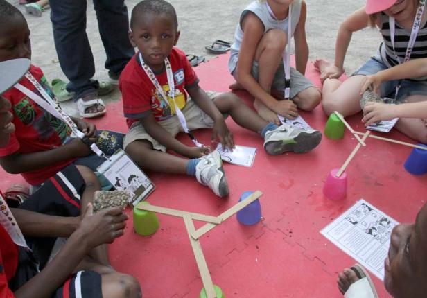 Kinder sitzen auf dem Boden und bauen mit Bechern und Holzstäben eine Konstruktion.