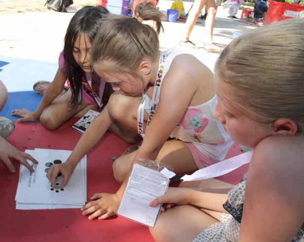 Drei Mädchen sitzen auf dem Boden und beschäftigen sich mit einem Arbeitsblatt.