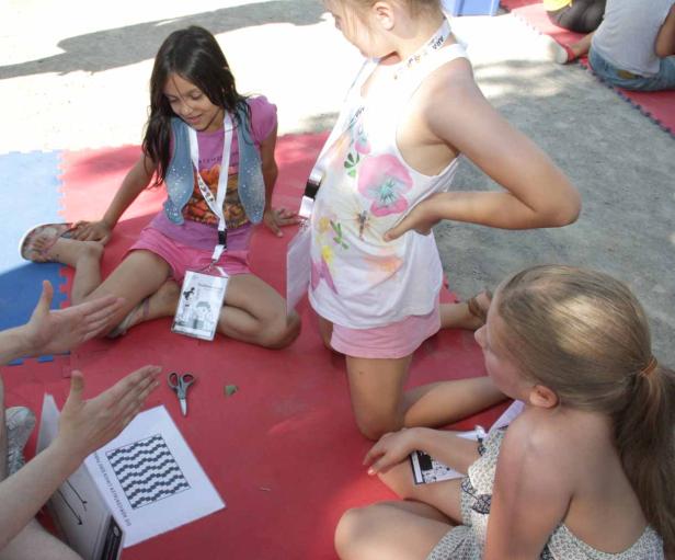 Drei Mädchen sitzen auf dem Boden und basteln mit Papier und Scheren.