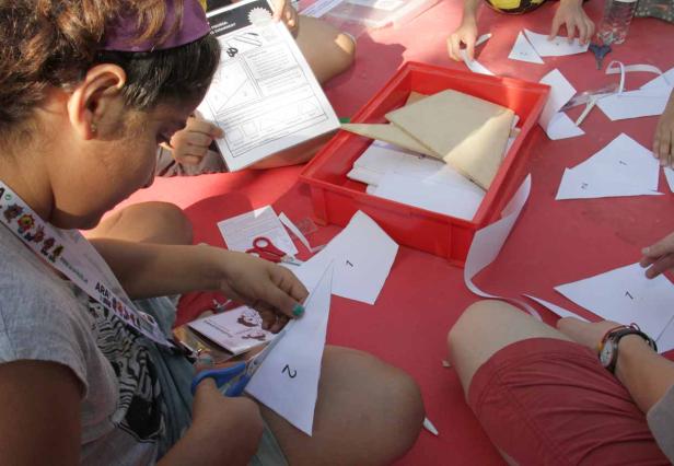 Kinder sitzen an einem roten Tisch und schneiden Papier für ein Bastelprojekt.