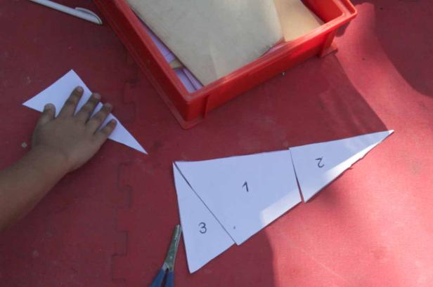 Ein Kind bastelt mit Papier und einer Schere ein Dreieck, das in drei Teile geteilt ist.