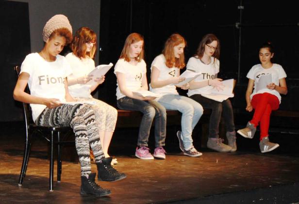 Eine Gruppe junger Schauspielerinnen sitzt auf einer Bühne und liest ihre Drehbücher.