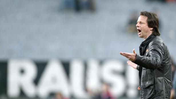 Ein Fußballtrainer gestikuliert auf dem Spielfeld und ruft Anweisungen.