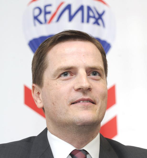 Ein Mann im Anzug vor dem Logo von RE/MAX.