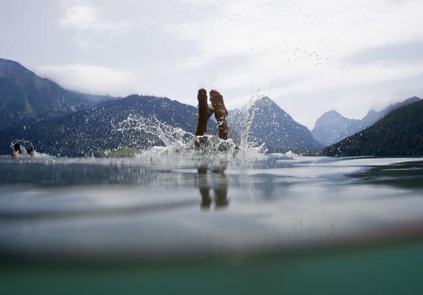 Eine Person springt mit den Füßen zuerst in einen Bergsee.