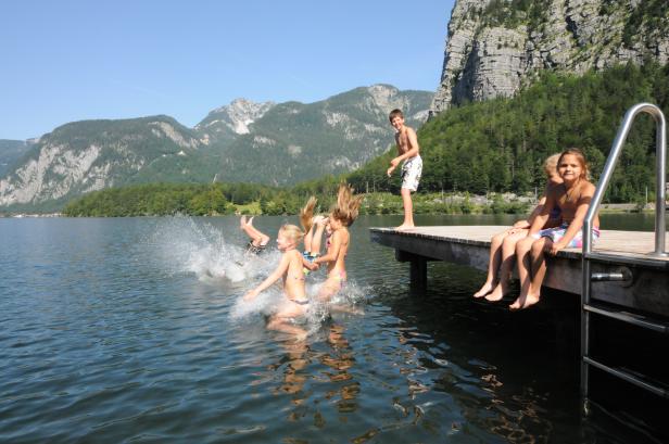 Eine Gruppe Kinder springt von einem Holzsteg in einen Bergsee.