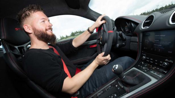 Ein Mann mit Bart fährt einen Sportwagen mit roter Innenausstattung.
