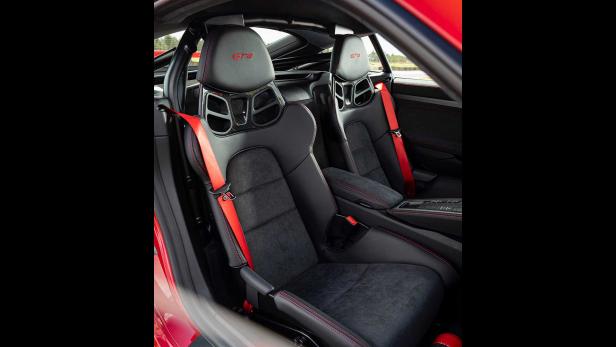 Das Interieur eines roten Porsche GT4 mit schwarzen Sportsitzen und roten Sicherheitsgurten.