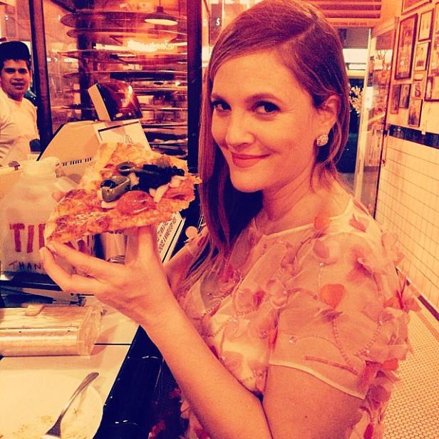 Drew Barrymore hält ein großes Stück Pizza in einem Restaurant.