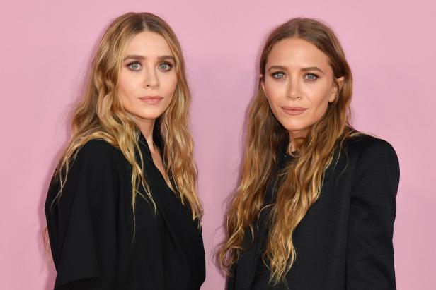 Die Zwillinge Mary-Kate und Ashley Olsen posieren vor einem rosa Hintergrund.