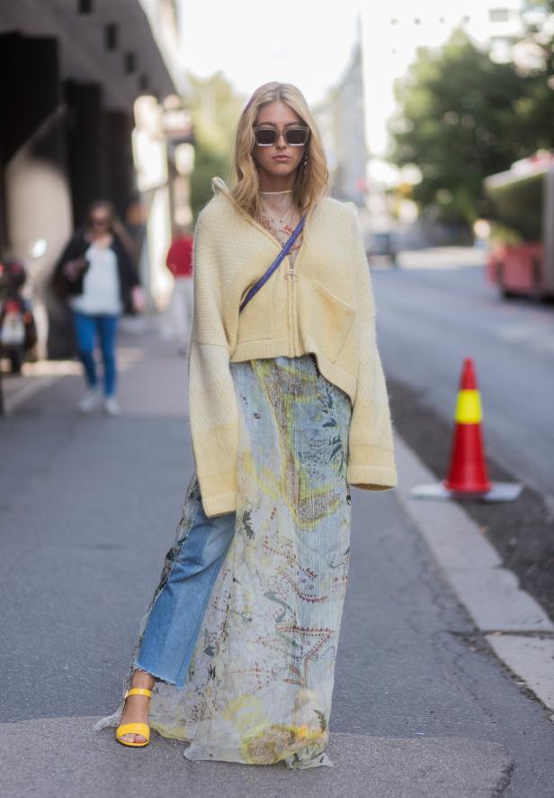 Eine Frau mit Sonnenbrille trägt einen gelben Cardigan und ein langes, gemustertes Kleid.