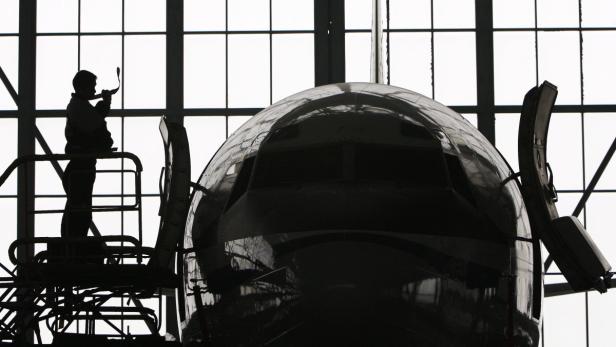 Ein Arbeiter steht auf einem Gerüst vor dem Rumpf eines Flugzeugs.