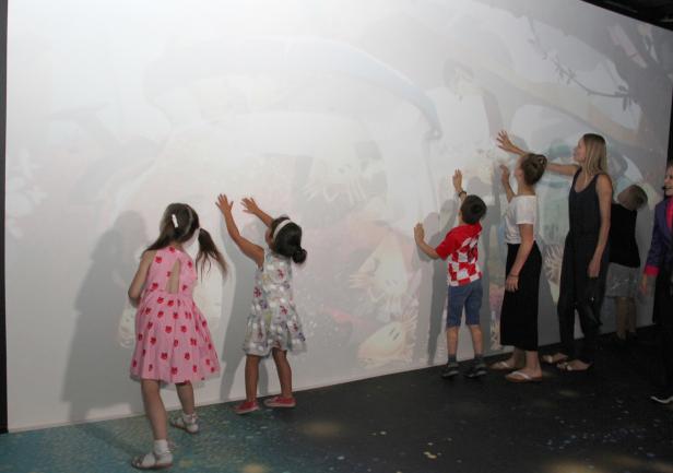Kinder und eine Frau interagieren mit einer interaktiven Projektion an einer Wand.