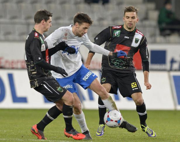 Drei Fußballspieler kämpfen um den Ball auf dem Spielfeld.