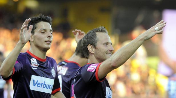 Zwei Fußballspieler winken dem Publikum zu.