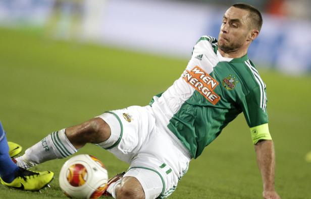 Ein Fußballspieler in grün-weißem Trikot rutscht auf dem Rasen nach dem Ball.