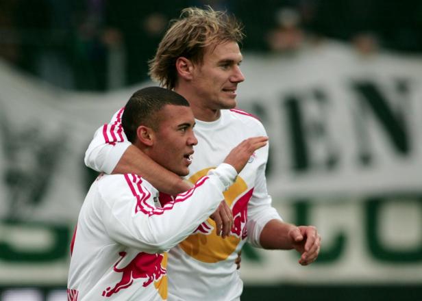 Zwei Fußballspieler in weißen Trikots mit rotem Logo umarmen sich.