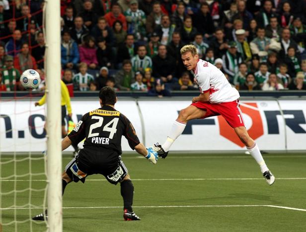Ein Fußballspieler schießt den Ball, während der Torwart versucht, ihn abzuwehren.