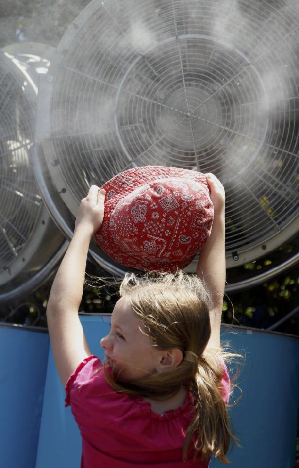 Ein Mädchen hält einen roten Hut in die Luft, während es vor großen Ventilatoren steht.