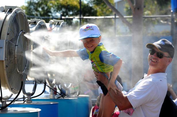 Ein lächelnder Junge wird von einem Mann vor einem Ventilator mit Wassernebel gehalten.