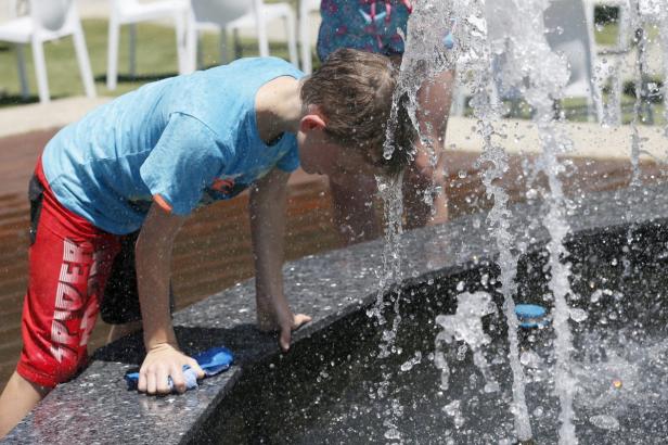 Ein Junge spielt an einem heißen Tag mit Wasser in einem Springbrunnen.
