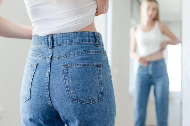 Eine Frau probiert vor einem Spiegel eine blaue Jeanshose an.