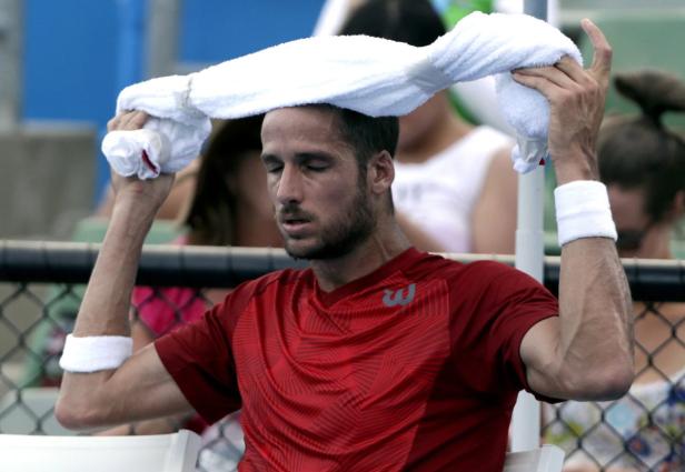 Ein Tennisspieler wischt sich mit einem Handtuch den Schweiß von der Stirn.
