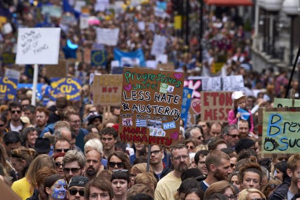 Eine große Menschenmenge demonstriert mit Schildern gegen Hass und Sparmaßnahmen.