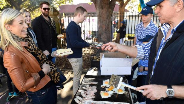 Menschen stehen um einen Grill mit Eiern und Speck.