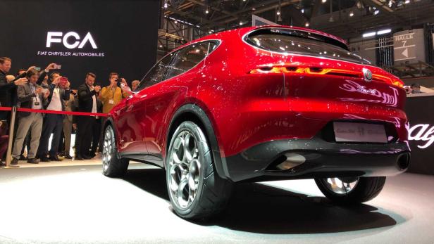 Der rote Alfa Romeo Tonale wird auf einer Automobilmesse von Menschen fotografiert.
