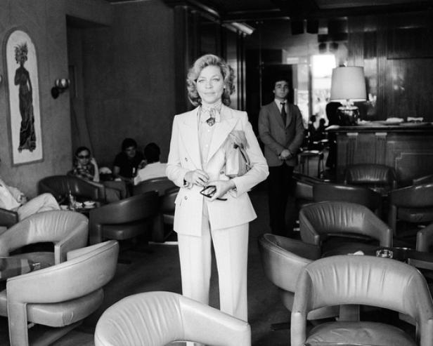 Lauren Bacall in einem Hosenanzug in einem belebten Innenraum.