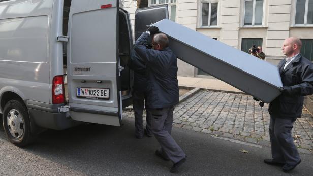 Mitarbeiter tragen einen langen, grauen Gegenstand aus einem Lieferwagen.