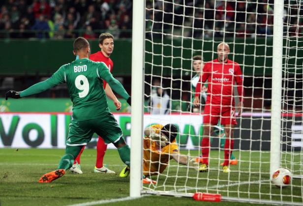 Ein Fußballspieler in Grün schießt aufs Tor, während der Torwart versucht, den Ball zu halten.