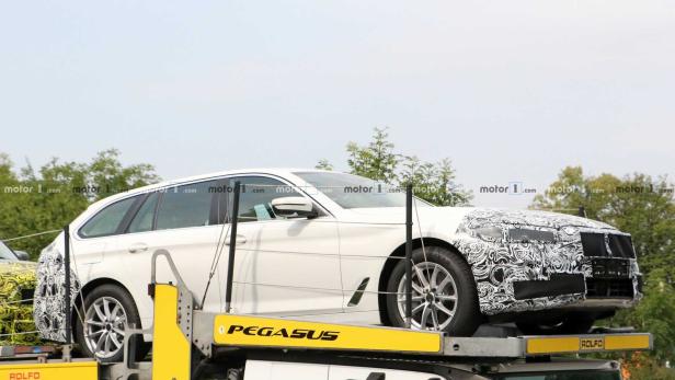 Ein weißer BMW Kombi mit getarnter Front steht auf einem Anhänger.