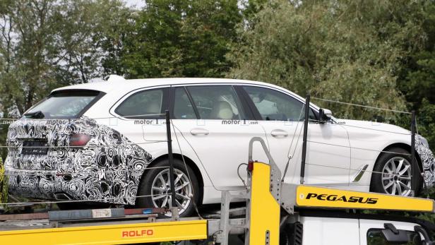 Ein weißer BMW Kombi mit teilweise getarnter Karosserie auf einem Anhänger.