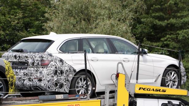 Ein weißer BMW Kombi auf einem Anhänger, teilweise mit Tarnmuster beklebt.