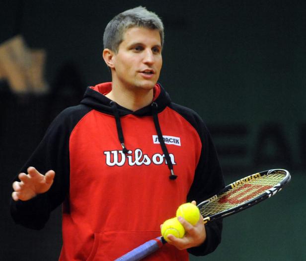 Ein Mann im roten Wilson-Hoodie hält Tennisschläger und Bälle.