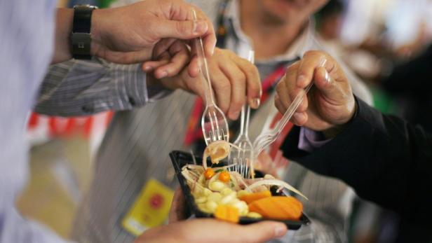 Mehrere Personen essen Ceviche von einem schwarzen Teller mit Plastikgabeln.