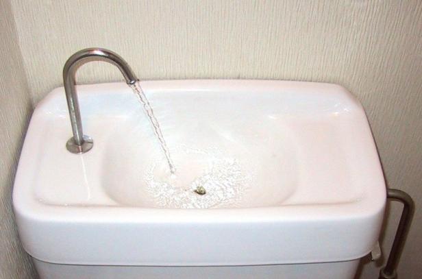 Ein Waschbecken auf einem Toilettenspülkasten mit laufendem Wasserhahn.