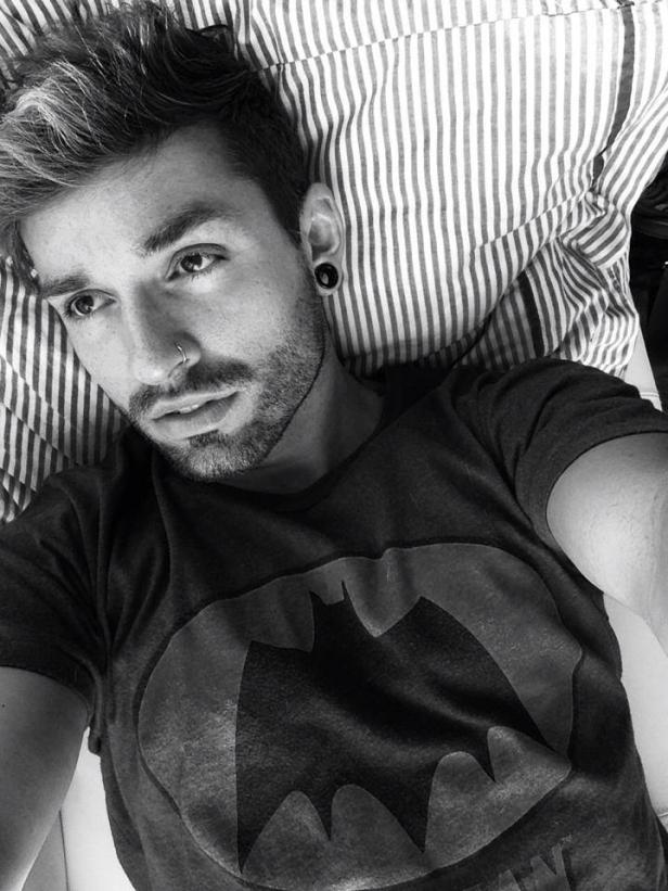 Ein Mann mit Nasenring und Batman-T-Shirt liegt auf einem gestreiften Kissen.