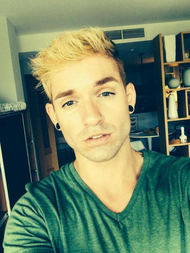 Ein Mann mit blond gefärbten Haaren und einem grünen T-Shirt macht ein Selfie.